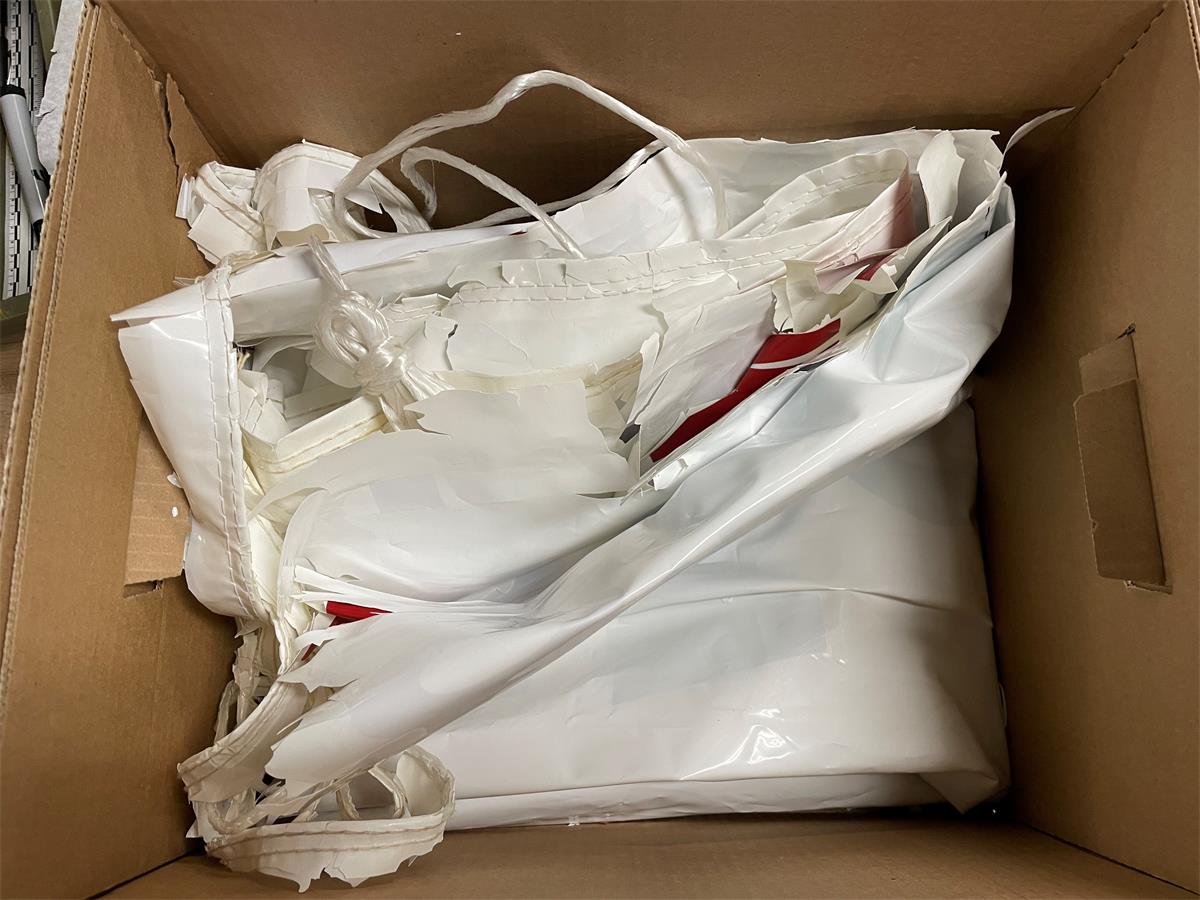 White plastic banner crumpled into brown cardboard box, is shattering.